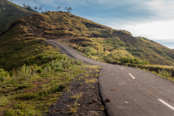 Curved mountain road winding through lush green hills at sunrise. Peaceful, remote, and perfect for travel, adventure, or nature-themed projects with space for text overlay.