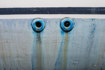 Detail of two blue circular boat drains with rust and water streaks on a worn hull surface