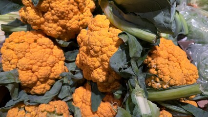 Close-up of orange organic cauliflower with green leaves — natural vegetables for a healthy...