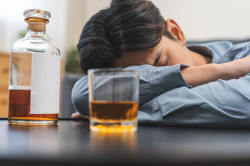 Health care alcoholism drunk, fatigue asian young man holding glass of whiskey, depressed male drink booze, sleep on table at home. Treatment of alcohol addiction, suffer abuse problem alcoholism.