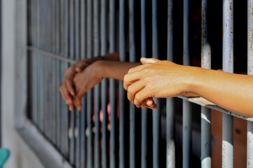 hands of a prisoner behind prison bars on black background