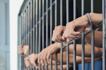hands of a prisoner behind prison bars on black background