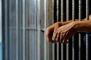 hands of a prisoner behind prison bars on black background