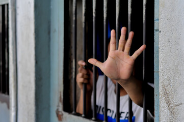 hands of a prisoner behind prison bars on black background