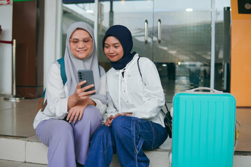 Two Asian hijab woman resting on train station stairs, enjoying a light conversation while...