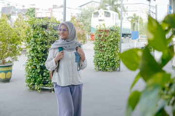 Young Asian woman in hijab standing at train station entrance hall with backpack, ready for journey