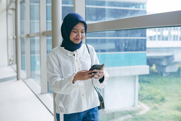 Asian woman in hijab walking through airport corridor, holding passport and smartphone, ready for...
