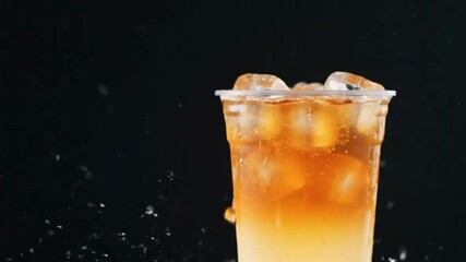 Iced beverage in a plastic cup with condensation ice  a gradient from light to dark Black backdrop water droplets visible
