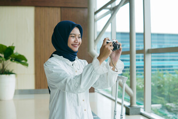 Asian woman in hijab taking photos of the airport atmosphere with a pocket camera, capturing...
