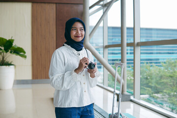 Asian woman in hijab taking photos of the airport atmosphere with a pocket camera, capturing...