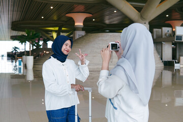 Two Asian women in hijab taking photos of each other at the airport, enjoying their time before...