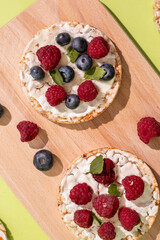 Rice cakes with different types garnish fruits, on green background. Healthy colorful food. Crispy puffed rice cakes with fruit and honey