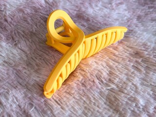 Vibrant yellow claw clip for hair, placed on a soft, pink textured background.