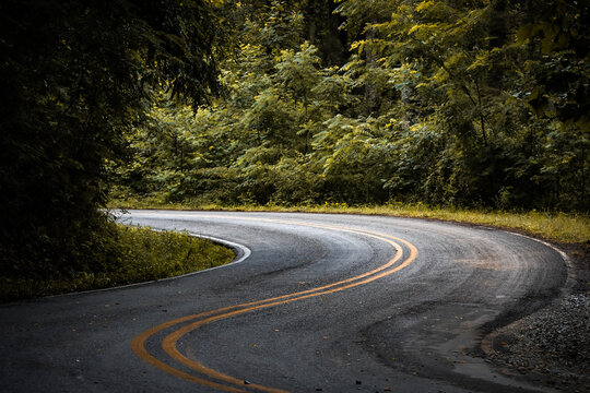 a winding mountain road with sharp curves and elevation changes. beautiful mountain pass scenic drive surrounded by forest background.