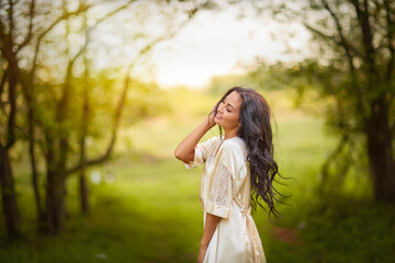 A woman in a white dress stands in an autumn forest. She is naked and hugs herself with her arms.