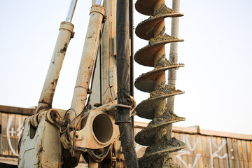 Close-up of an industrial drilling machine with auger bit coated in soil, used for ground...