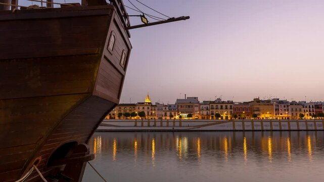 Timelapse sequence from the banks of the Guadalquivir River, capturing the transition from daylight to evening over Seville&rsquo;s traditional Triana neighborhood. The city lights reflect in the water as t
