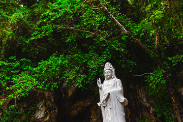 Fototapeta premium Serene white statue of guanyin in lush green forest