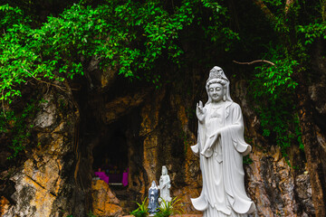 Serene white statue of asian deity in lush natural cave setting