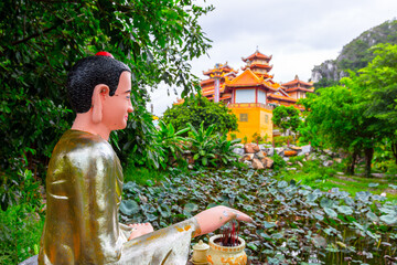 Buddha statue by lotus pond and traditional temple in lush greenery