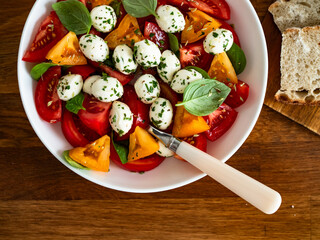 Caprese salad - tomatoes, basil leaves and mozzarella balls on wooden background