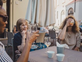 Diverse mature women sharing coffee at sunny outdoor cafe, laughing and conversing, representing...