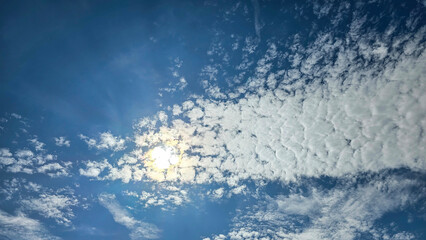 Blue sky with scattered clouds and sunlight shining through, natural sky texture and background.