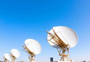 Satellite Dishes Arrayed: A collection of satellite dishes, capturing the sky with precision, ready to receive and transmit signals under a clear, vibrant blue canvas.