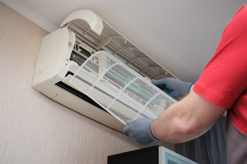 Close-up of a person removing the dust filter from a wall-mounted split air conditioner for maintenance.