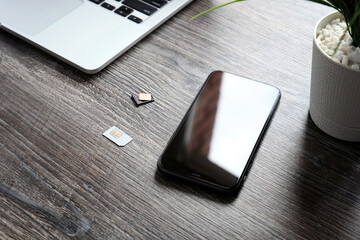 Two SIM cards, a modern smartphone and a laptop are lying on a wooden table.