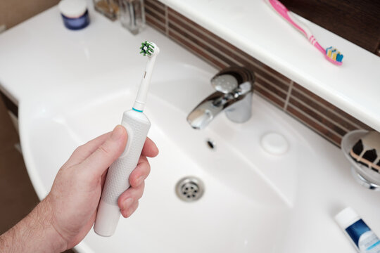 Close-up a mans hand holding electric toothbrush against bathroom background.