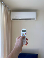A man's hand turns on an air conditioner using a remote control in an apartment or house.