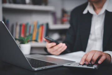 Businessman using calculator and smartphone at desk with laptop, symbolizing financial planning, business accounting, data analysis, modern finance, budgeting, small business management.