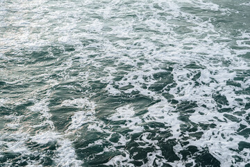 Abstract aerial view of swirling sea foam on deep green water