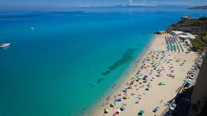 Aerial view of tourists sunbathing and swimming in the turquoise Tyrrhenian Sea at Tropea beach,...