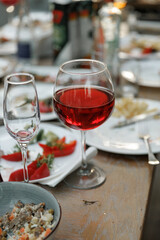 Red wine glass and snacks on a wooden table set for a casual meal. Plates with various appetizers accompany the centerpiece glass, creating a relaxed dining atmosphere.
