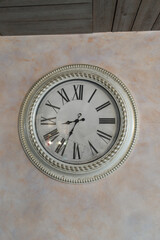 Vintage wall clock with a classic design featuring Roman numerals on a textured wall. The clock's...
