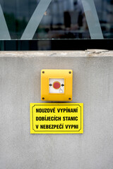 Emergency stop button with a red center and yellow casing mounted on a concrete wall. Below it, a...
