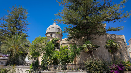 The dome and apse of the Norman Cathedral stand out against a clear blue sky, surrounded by the...