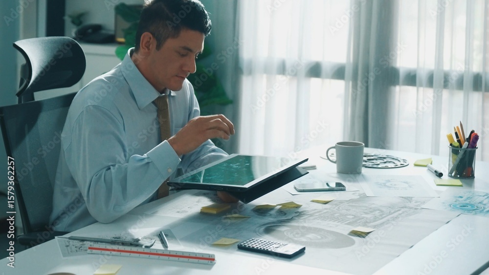 Poster professional engineer looking at phone while working on tablet with green screen at meeting table wi