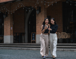 Two young businesswomen walking and using smartphone in urban background