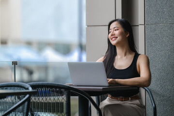 Young Asian Freelancer Working on Laptop in Outdoor Cafe, Enjoying City View