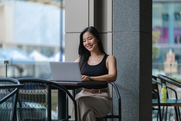 Young Asian businesswoman working remotely using laptop in outdoor cafe