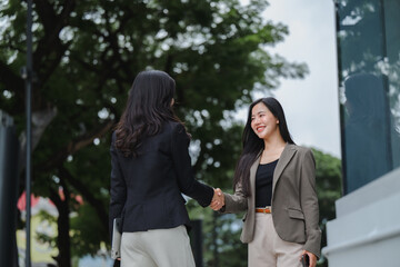 Two businesswomen shaking hands in front of modern office building