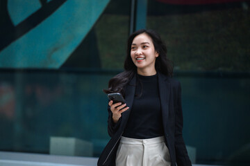 Young manager walking in the city using her smartphone and smiling
