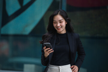 Smiling businesswoman using smartphone in front of modern building