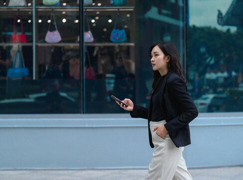 Businesswoman is walking on city street and using smartphone