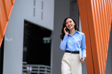 Young businesswoman walking and talking on phone while holding laptop