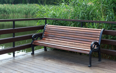 Wooden bench on a deck overlooking a calm river surrounded by lush green vegetation