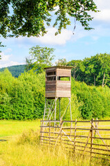 Wooden hunting tower standing on field edge surrounded by lush greenery and summer sky